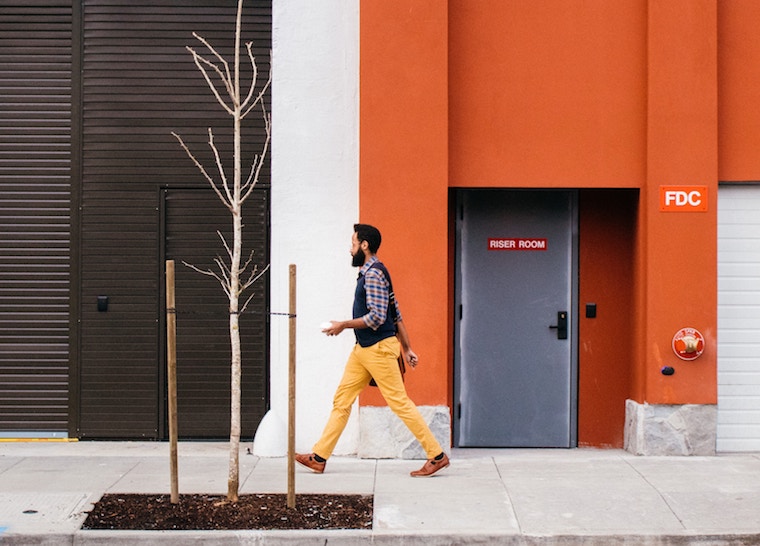 man walking street by bare tree