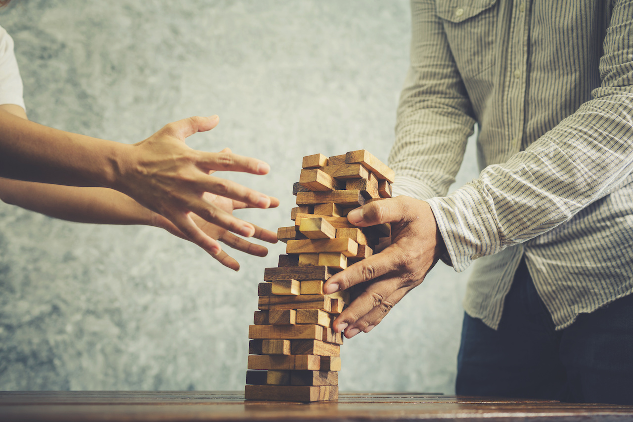 Business man and woman playing wood jenga game blocks in office studio.