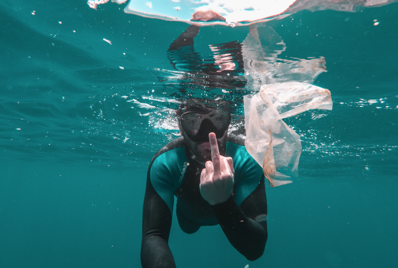 Photograph of diver surrounded by plastic, flipping the camera off