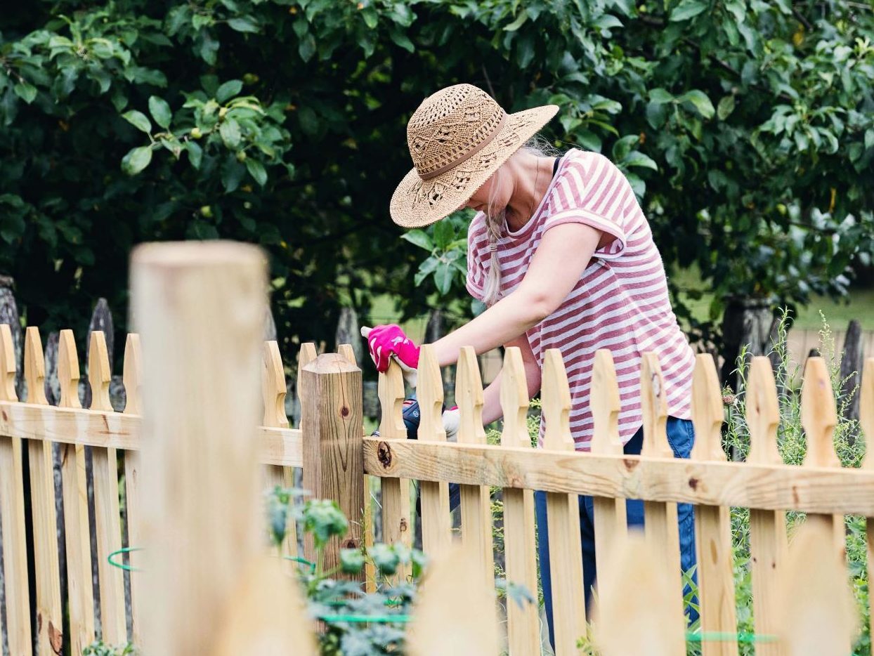 woman working in garden by wooden fence