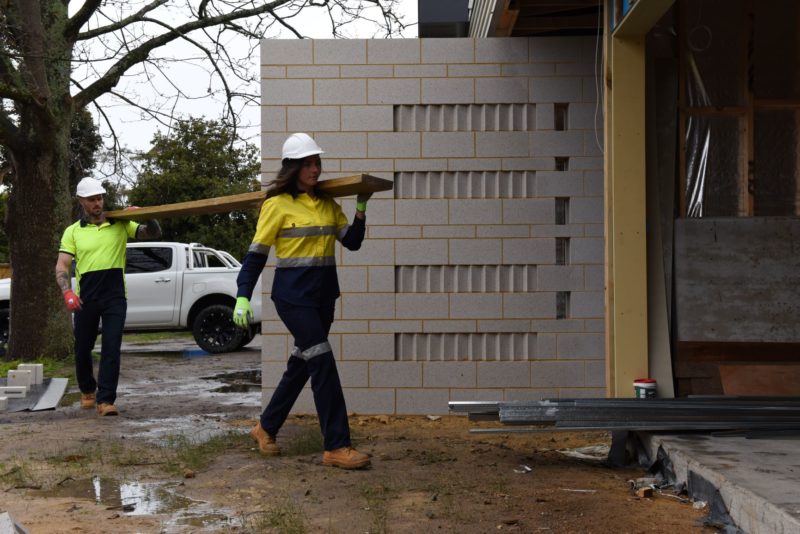 Two construction workers carrying a plank of wood on iste