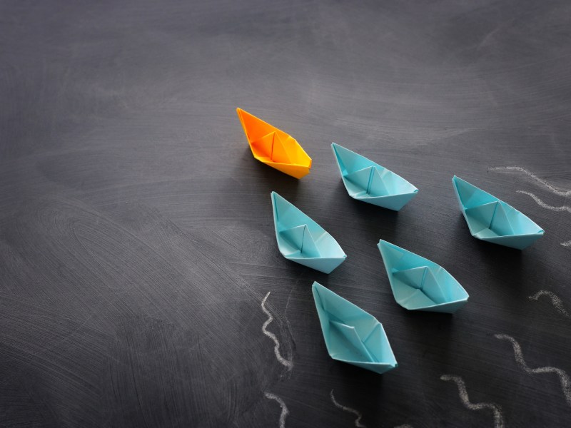 Leadership banner concept with paper boat on blackboard background. One leader ship leads others