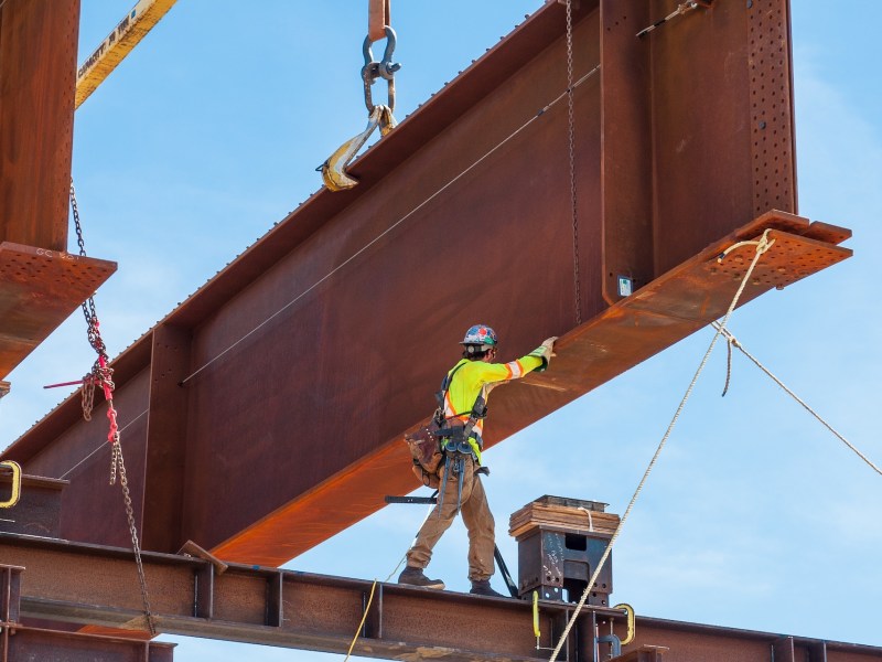Steel worker positioning a steel girder with 3 meter wide flange on temporary supports to bolt in the next section of bridge girder.