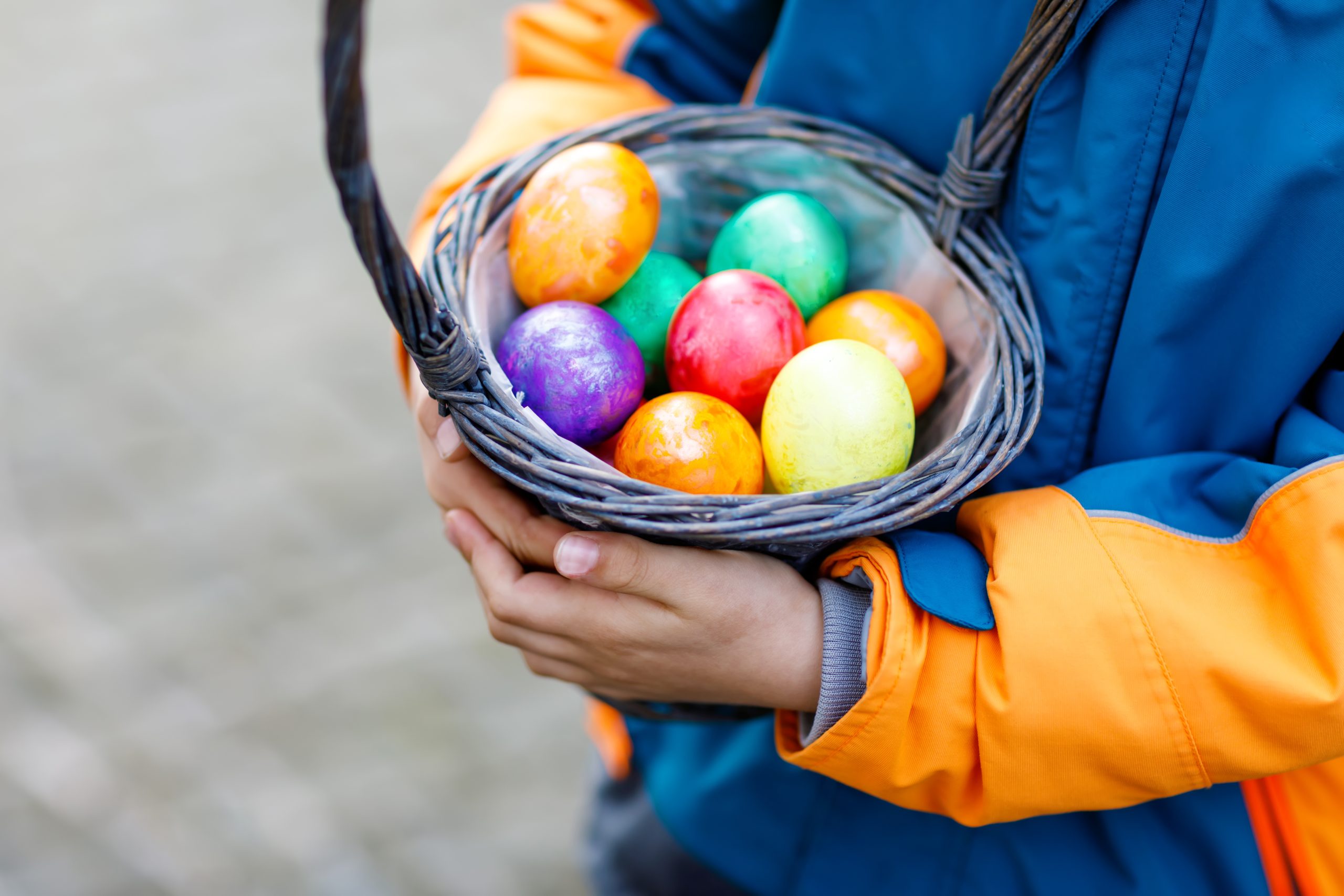 Close-up of hands of little child with colorful Easter eggs in basket. Kid making an egg hunt. child searching and finding colorful eggs in domestic garden. Old christian and catholoc tradition