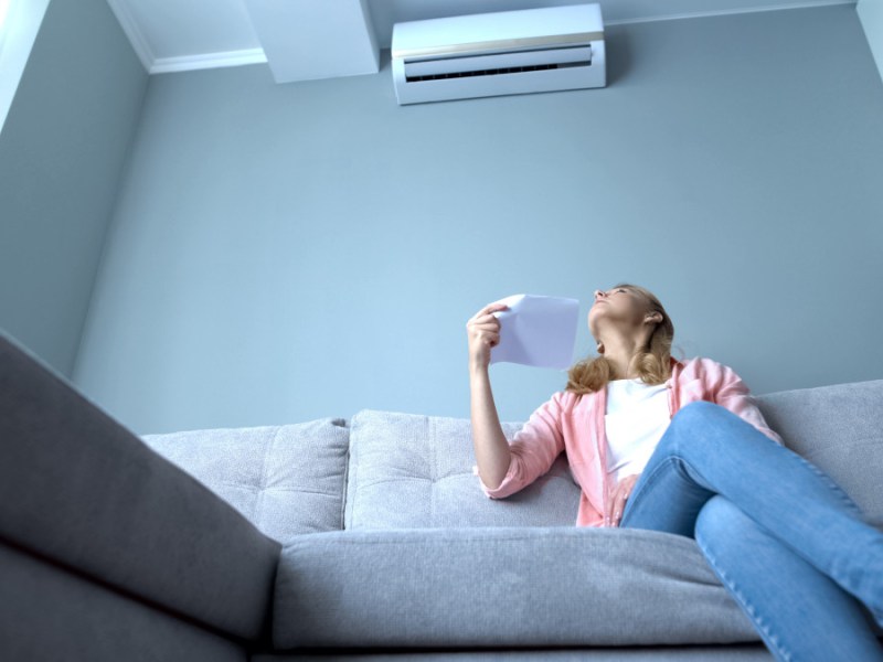 Woman looking at broken air conditioner sitting on couch, suffer