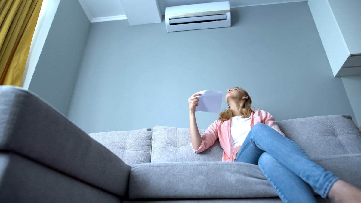 Woman looking at broken air conditioner sitting on couch, suffer
