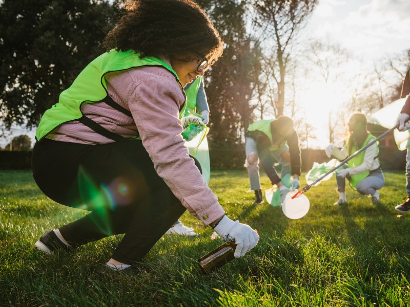 Group of friends during a volunteer garbage collection event in a park at sunset - Millennial having fun together - Happy people cleaning area with bags - Ecology concept