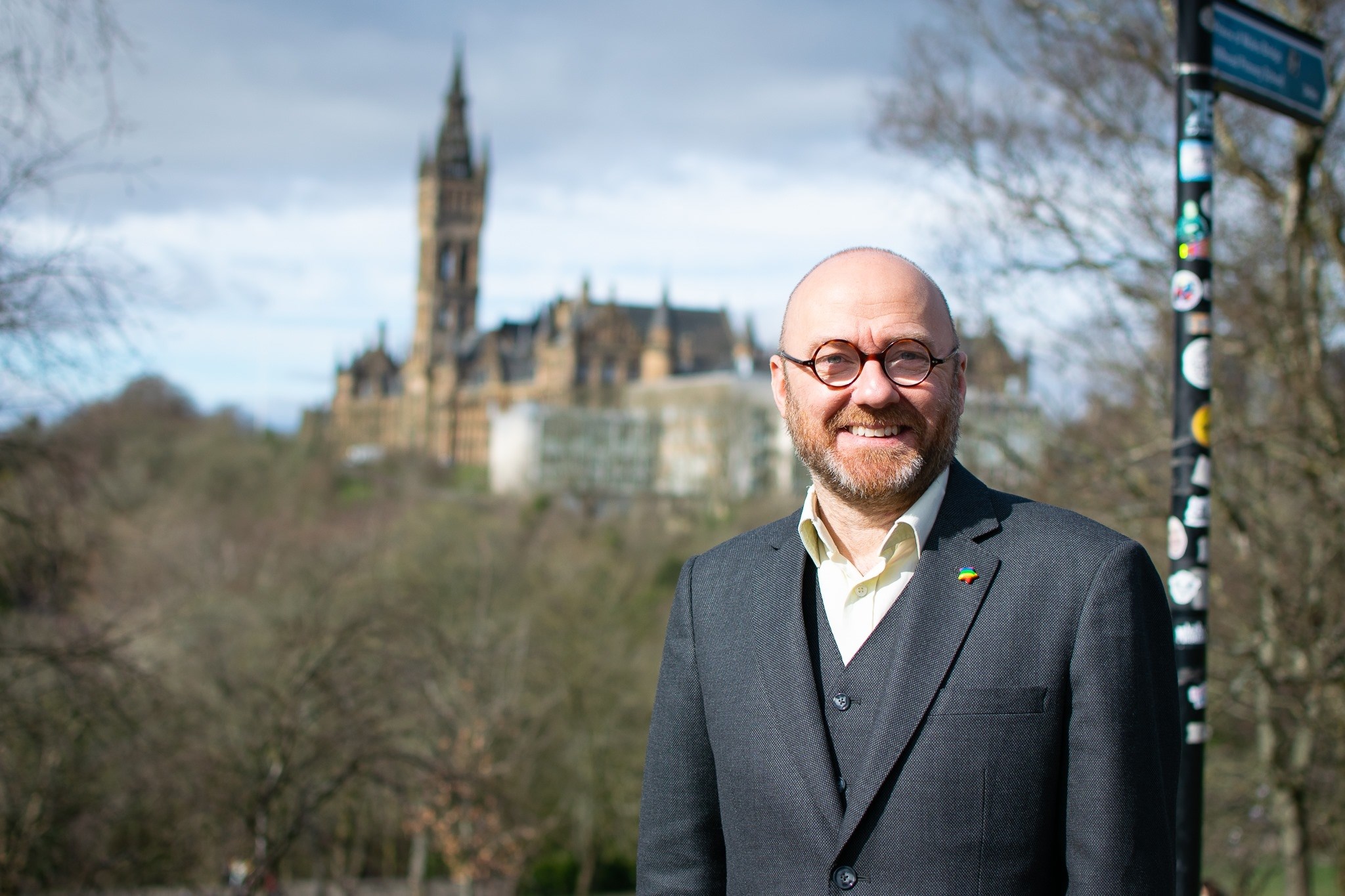 Man with glasses wearing a suit standing in front of a historical building