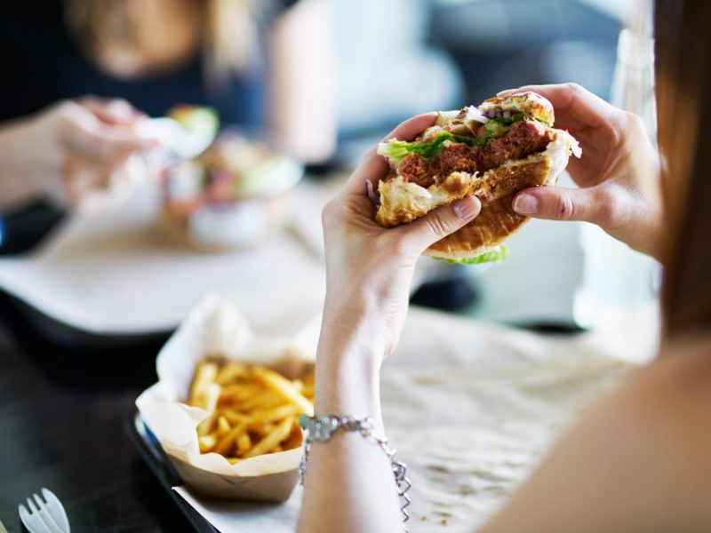 woman eating eating vegan meatless burger in restaurant