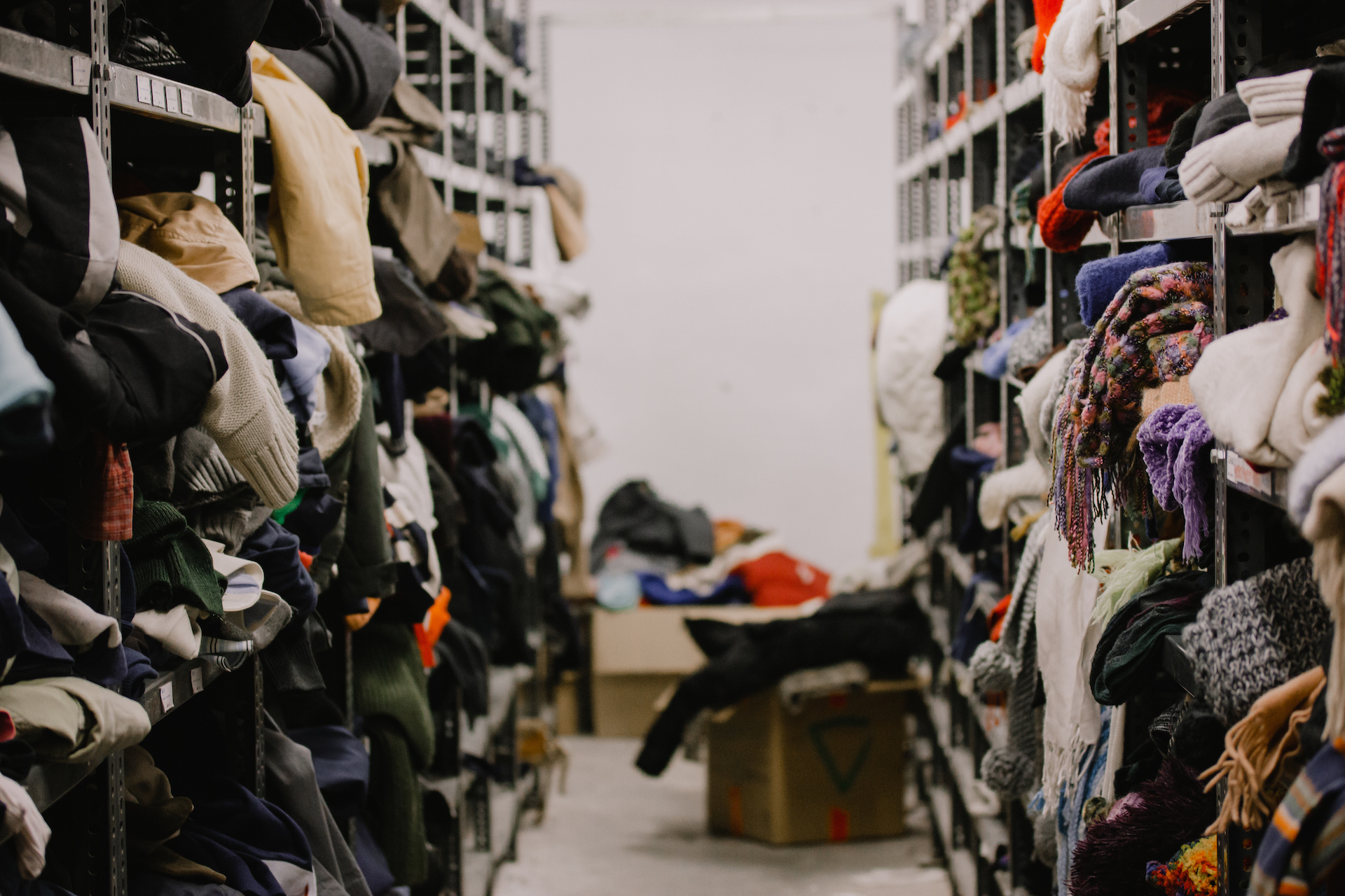 Humanitarian aid station, interior of industrial warehouse with used clothes for the poor, refugees, vulnerable people. Shelves, rows of clothes second hand. Stock clothing section collection.